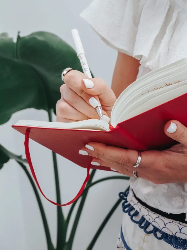 Close-up of two hands writing notes in a red hardcover notebook