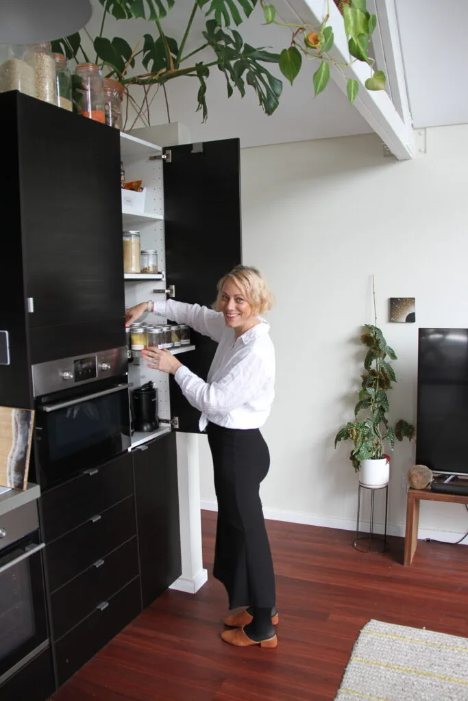 Kiah Bouchet placing a glass storage canister into an organised black kitchen pantry