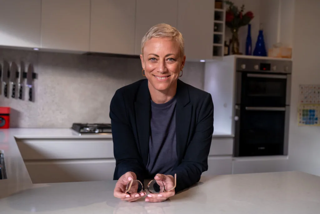 Kiah Bouchet smiling at a kitchen bench, holding her glasses, in a calm organised Perth home