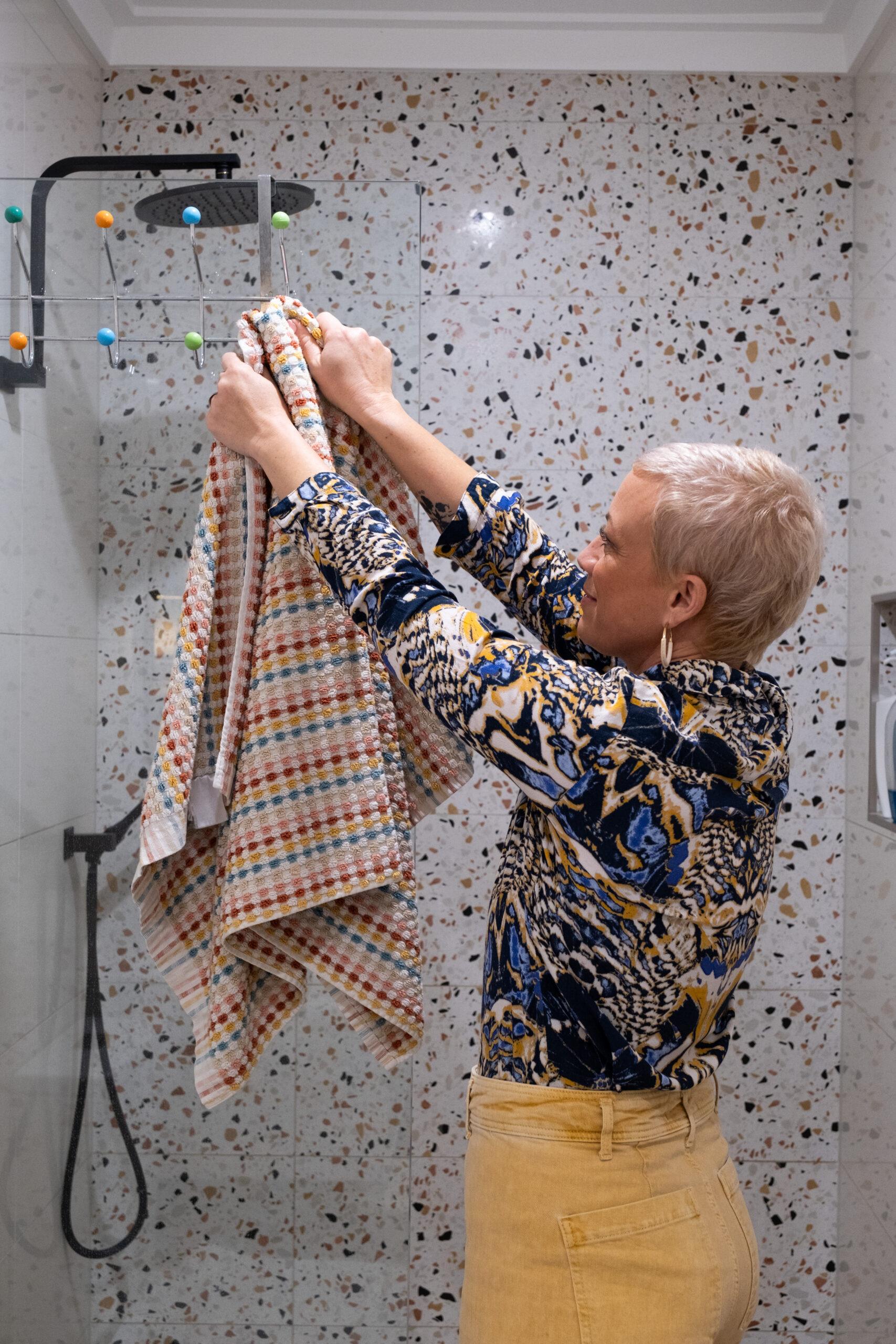 Kiah Bouchet tidying towels on a shelf in a terrazzo-tiled bathroom